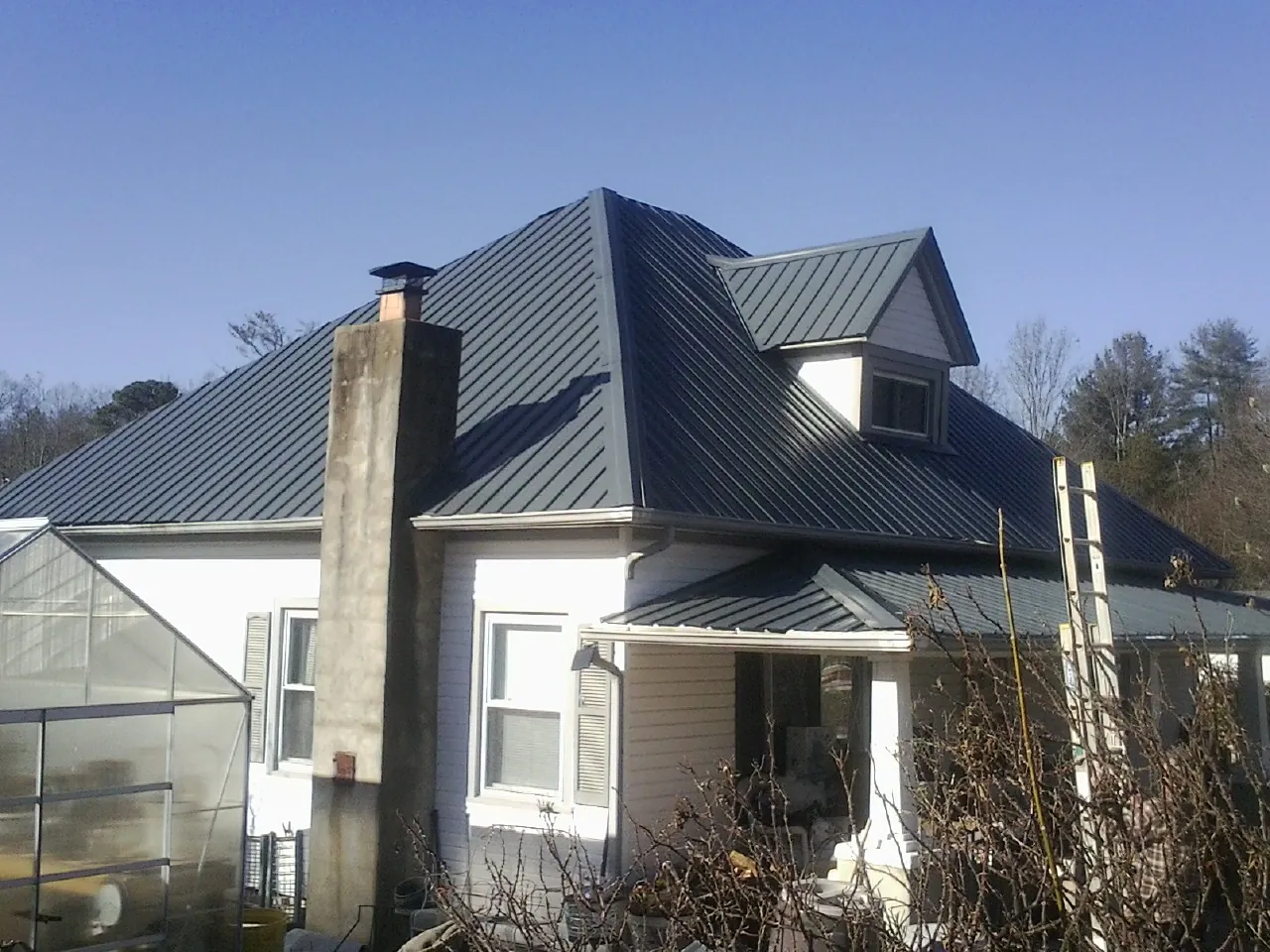 Dark blue standing seam metal roof on a white farmhouse with dormer — Slate & Tile Roof Repair by Roofing Brothers in Capron