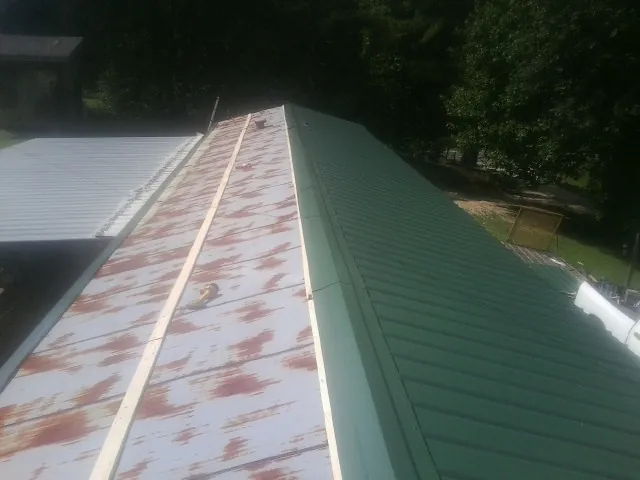 Old rusted panels beside newly installed green metal roofing — Wind Damage Roof Repair by Roofing Brothers in Capron