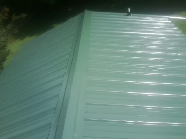New green metal panels meeting at the ridge of a roof — Flat Roof Repair work by our crew in Capron