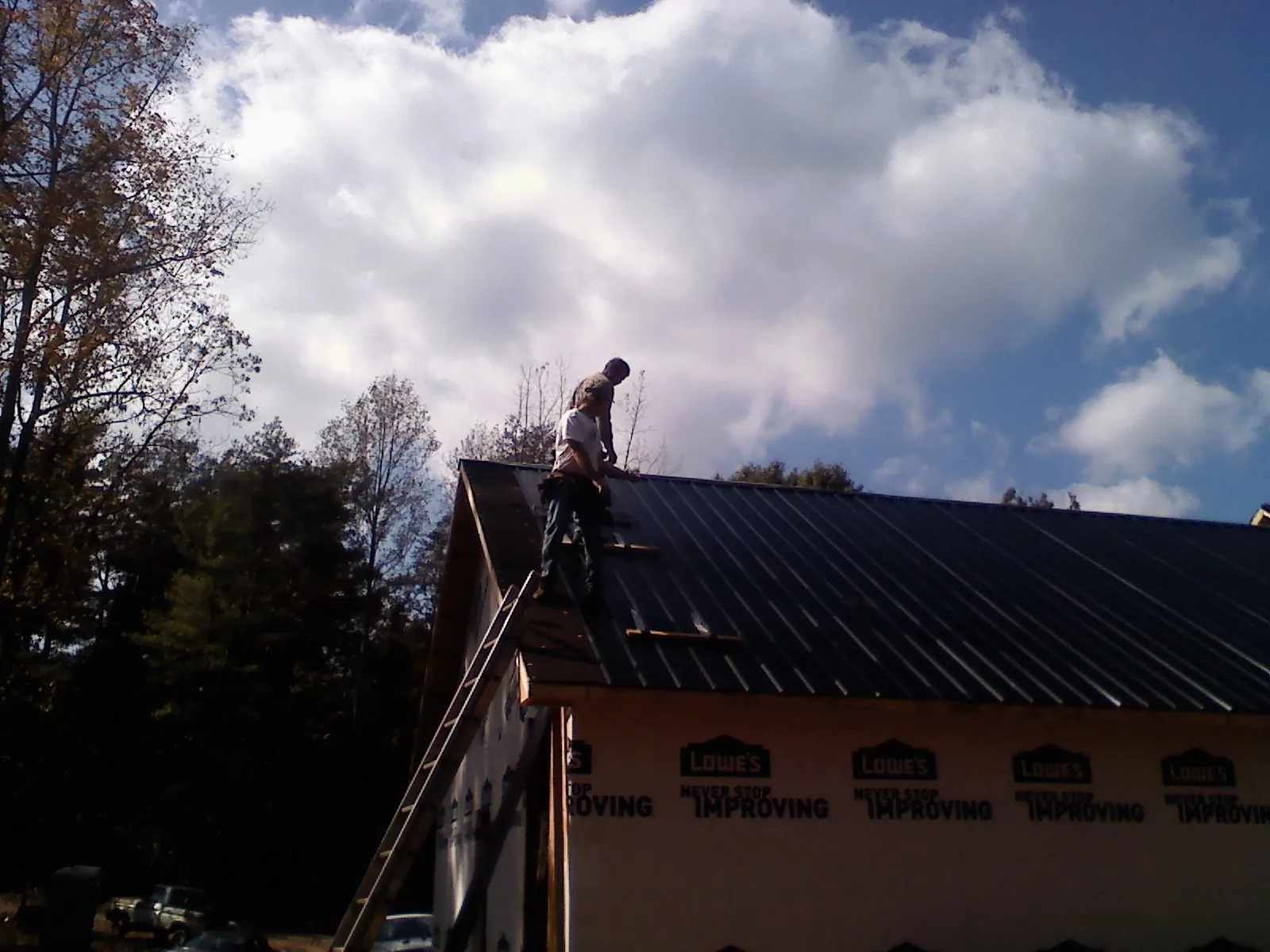 Roofer fastening dark metal panels high against a cloudy sky, from a Roof Inspection job in Capron